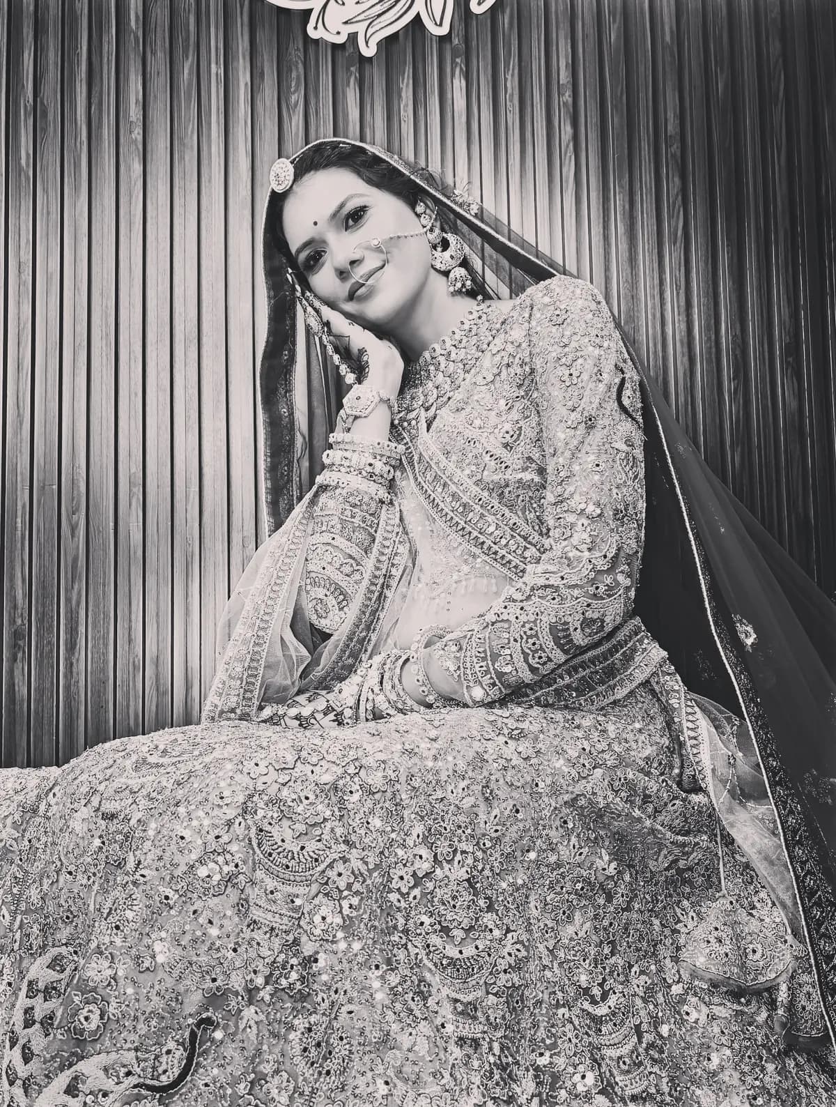 Black and white portrait of a bride seated in her lehenga, smiling softly