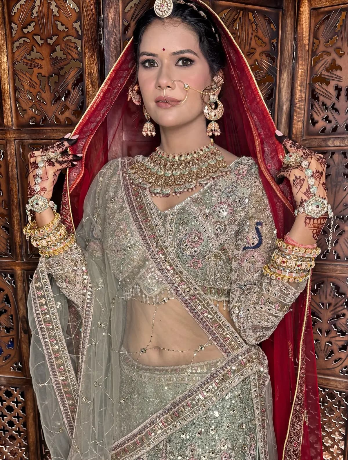 Full-length bridal portrait in a pastel lehenga against carved wooden screens