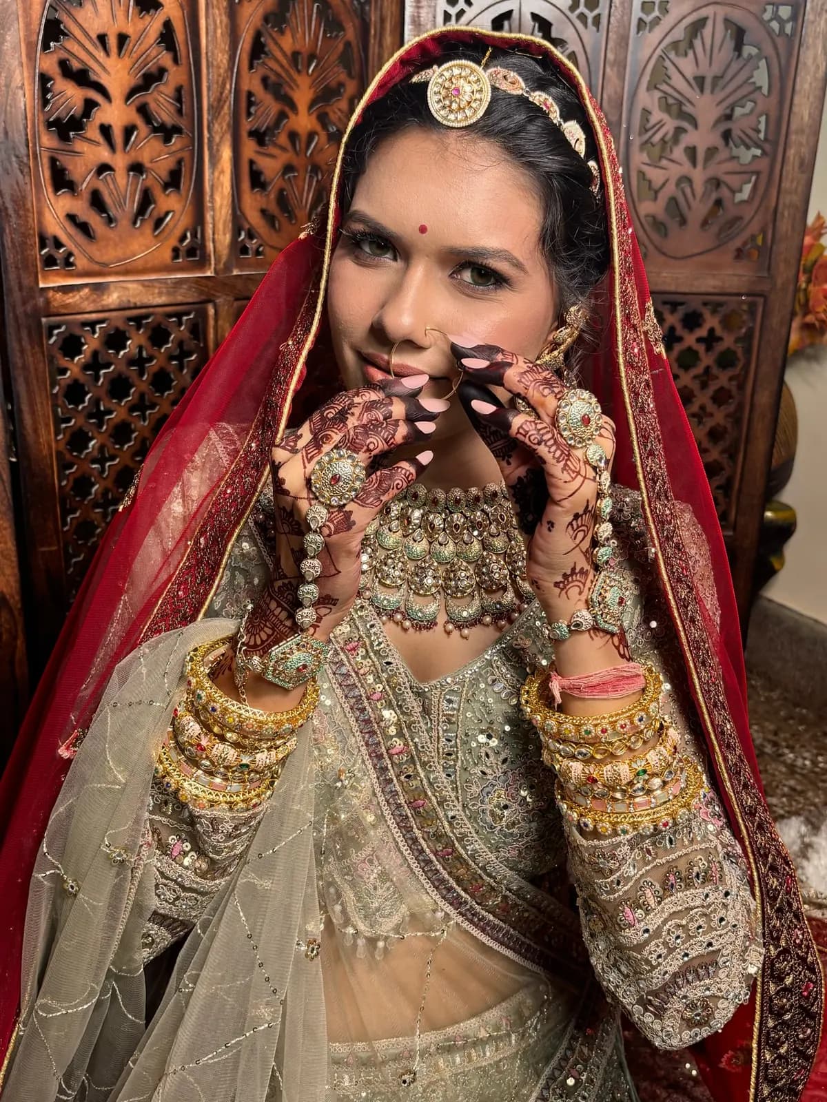 Bride framing her face with mehendi-adorned hands, maang tikka and kundan choker